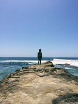 woman standing on rock looking out at the ocean 