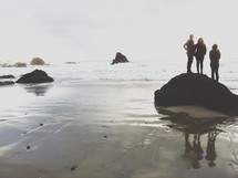 friends standing on a large rock on a beach
