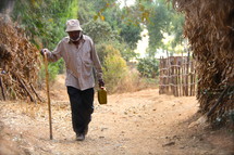 man with a cane walking on a dirt road 