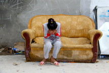 A young girl crying into her hands sitting on an old couch in a refugee camp in Northern Iraq