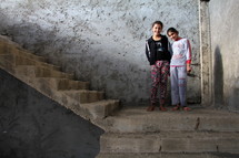 Two girls standing on concrete stairs in an abandoned building site. Now home to Azizi refugees in Kurdistan, Iraq