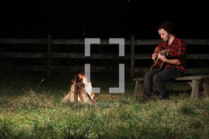 man playing a guitar by a campfire 