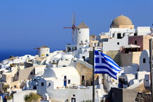 Flag of Greece flying in front of hillside village of homes.