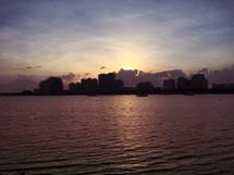 silhouettes of buildings across a lake at sunset 