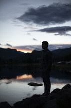 a man standing alone at the edge of a pond thinking and praying 