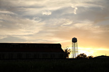 A barn and a water tower at sunset.