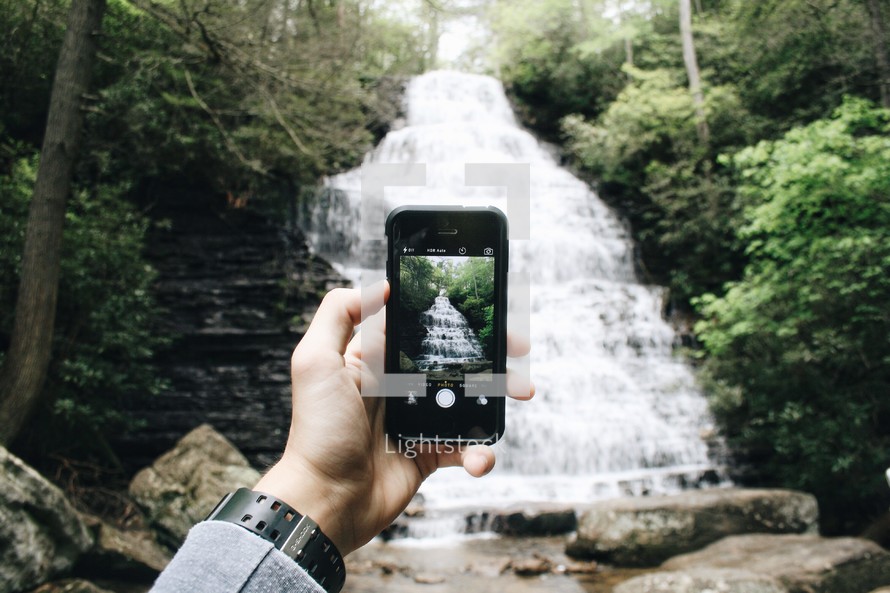 man taking a picture of a waterfall with his cellphone 