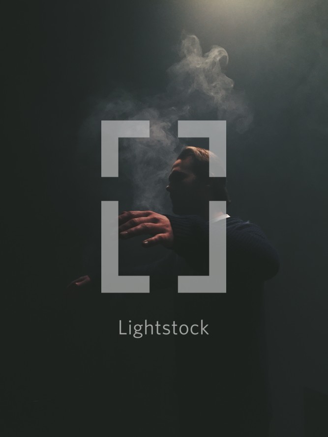 man with outstretched arms standing in smoke in darkness 