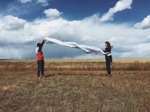 women holding a white sheet in a field 