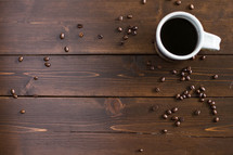 Coffee beans and a cup of coffee on a wooden surface.