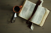 an open Bible, coffee mug, and reading glasses on a coffee table