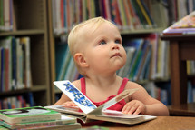 a toddler girl reading a book in a library 