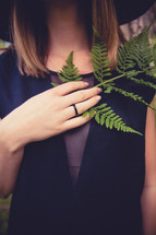 Woman holding a fern leaf to her chest.
