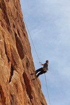 Woman rappelling after climbing steep mountain face 