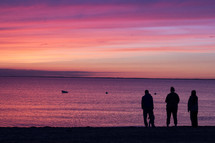 silhouettes of a family standing on a beach at sunset 
