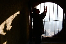 Chinese church leader holding his hands up in worship to God in front of a barred window