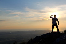 a man looking out at the view standing on a mountain top at sunrise/sunset