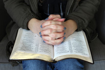 a woman with praying hands over the Bible in her lap 