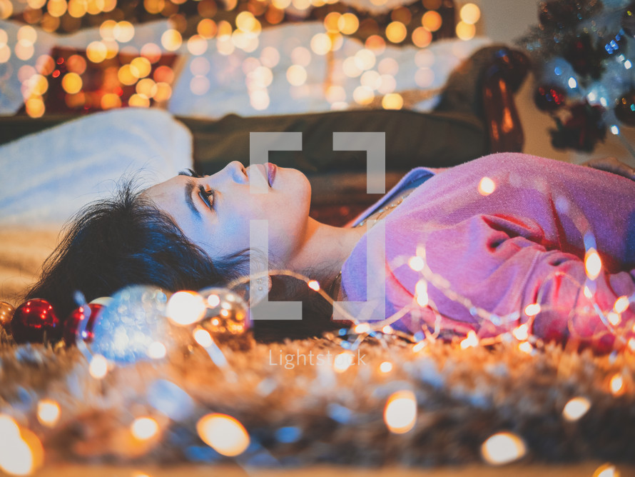 a woman lying on the floor next to glowing Christmas lights 