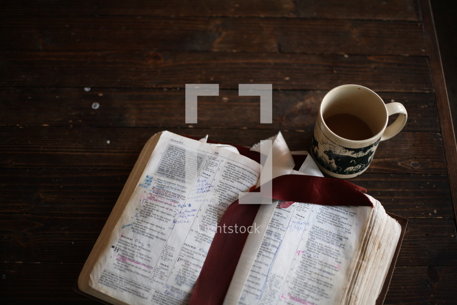 notes on the pages of a Bible and a coffee mug on a table 