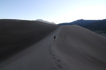 man walking up sand dunes 