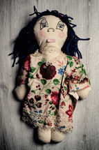 Handmade rag doll with button eyes and yarn hair is lying on a wooden background