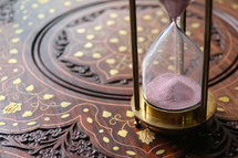 Sand measuring time running through an antique hour glass on oriental desk