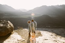 a couple snuggling under a blanket on a mountaintop 