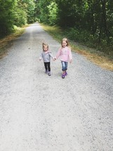 sisters holding hands walking on a gravel road 