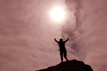 Silhouette of a man with his hands raised in the air in victory after climbing tall mountain