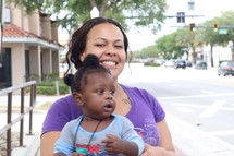 A woman holding a child on a city sidewalk.