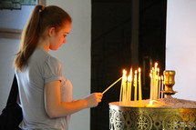 Young lady lighting a votive candle in an Eastern Orthodox Church