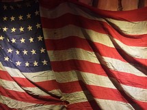 An old distressed American flag with faded stars and stripes hanging against old barnyard wood.