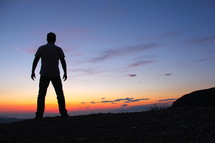 silhouette of a man standing on a mountain top at sunset / sunrise 