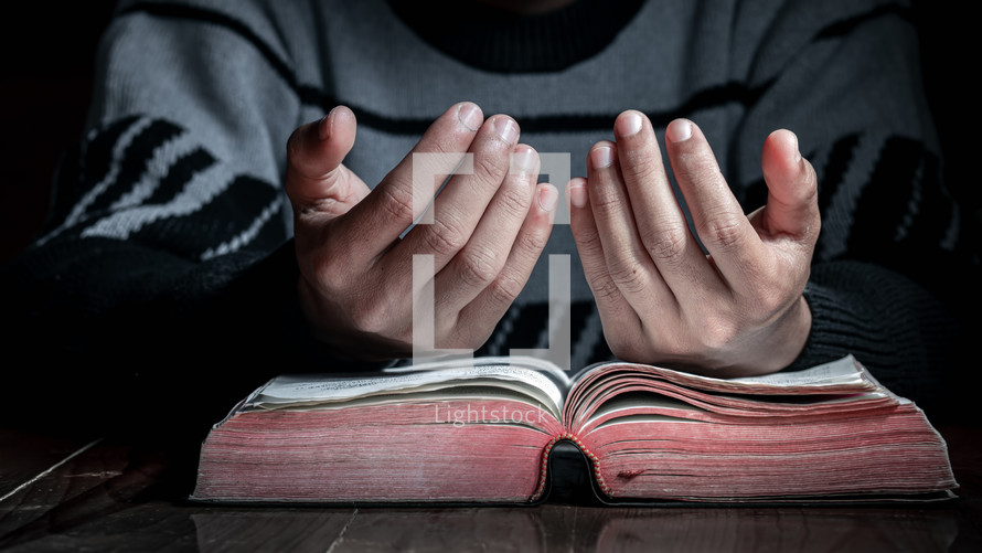 a male with lifted hands over a Bible in prayer 