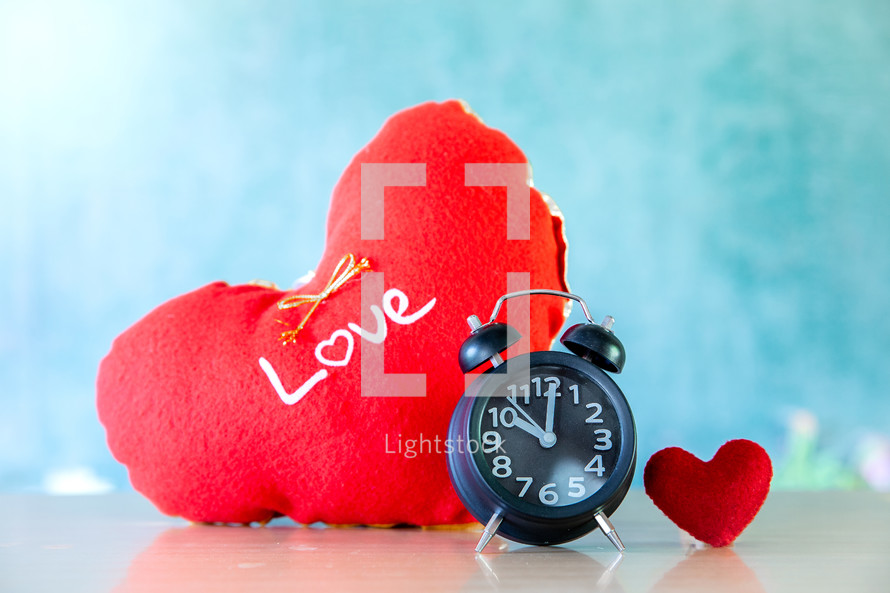 Alarm clock with red hearts on wooden table, valentine day background.