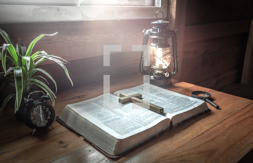 wooden cross on the pages of a Bible and lantern 