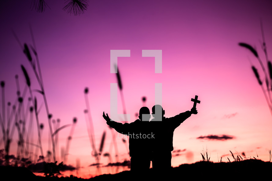 silhouettes of two boys holding a cross at sunset against a purple sky 