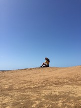 woman sitting at the top of a sand dune 