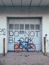 A bicycle leaning against an overhead door reading "Do not block" and "No parking."