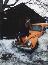 A woman sitting on an old Volkswagen Beetle.