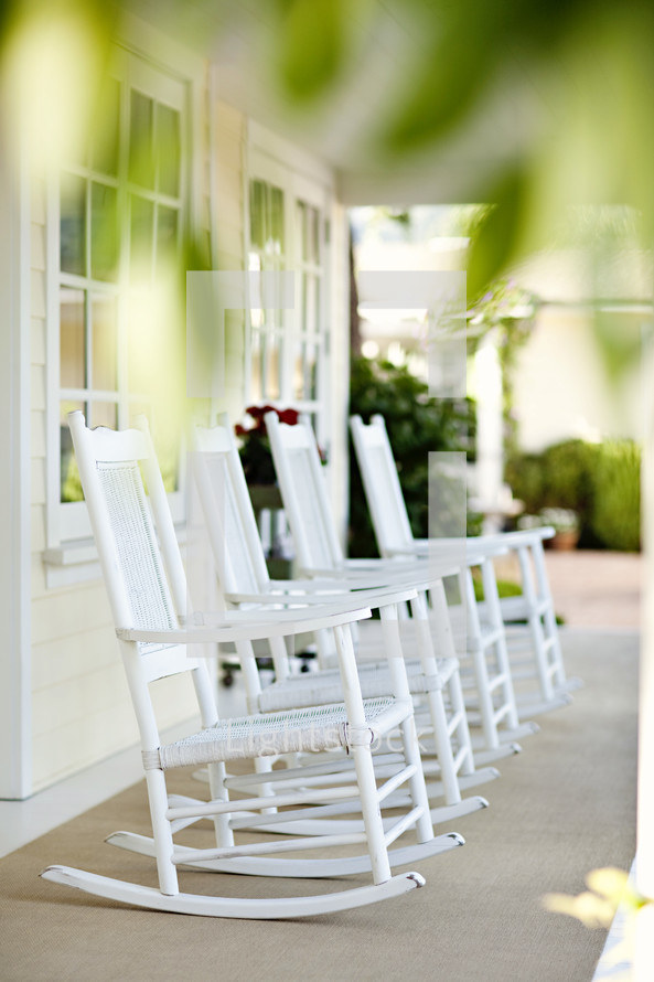 Four white rocking chairs sitting on front porch.