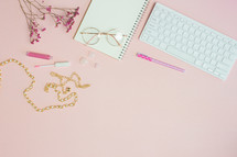 makeup and paper clips on a feminine pink computer desk 