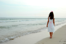 little girl in a dress walking on a beach 