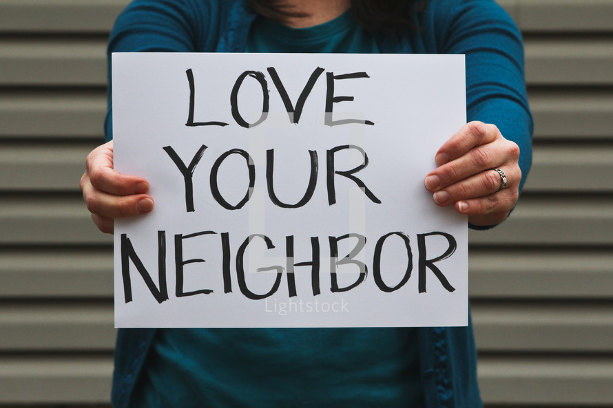 A woman holding up a sign that reads love your neighbor 