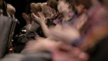 Impressed audience, made of Caucasian people sitting down, applauding, during a spectacular event. Close up hands only with no faces. Focus goes from back to front.