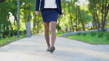 Legs of unrecognizable young business woman in formal wear walking in the green park alone. 