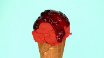 Strawberry ice-cream in waffle cone rotating on blue background and liquid wild berry topping pouring on it. Delicious isolated sweet dessert in studio.