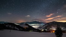 Panoramic view of beautiful starry night sky with stars and colorful clouds over winter mountains in snowy landscape time lapse
