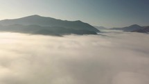 Aerial flight into the clouds in morning mountains landscape
